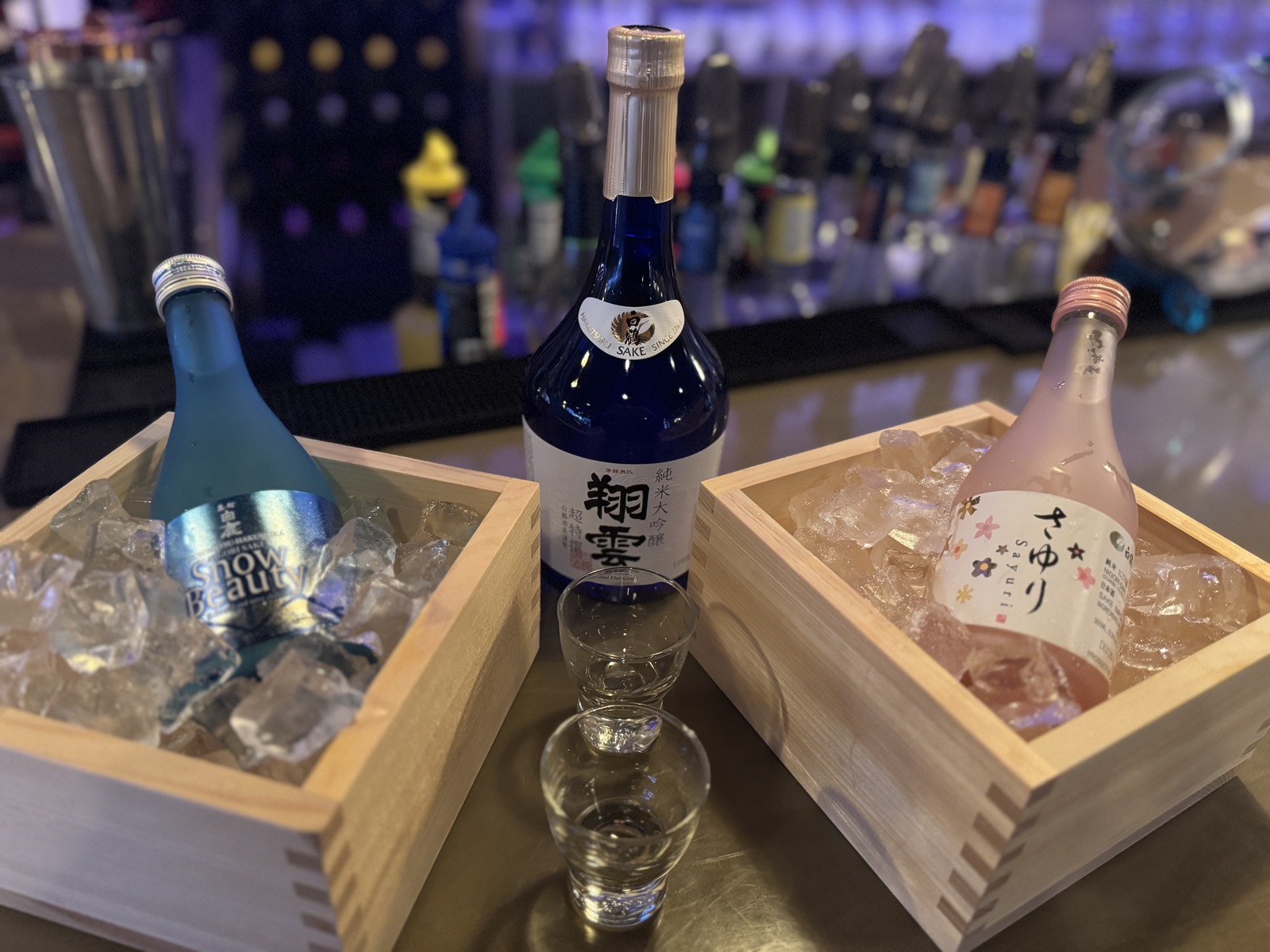 Four sake bottles chilling in cedar masu boxes of ice at the Sushikin sake bar